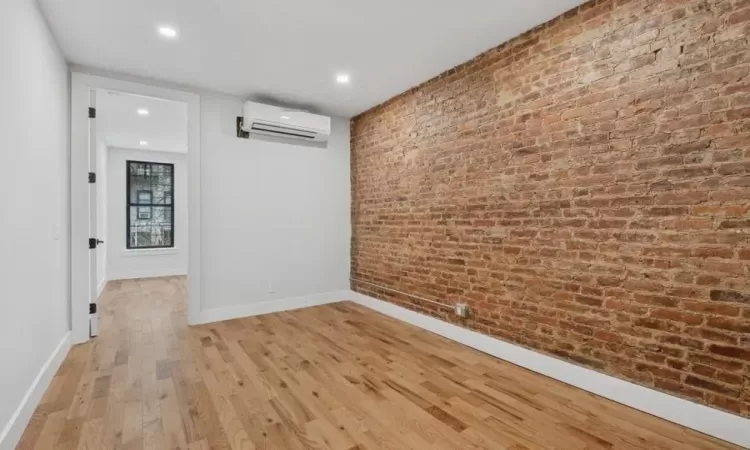 Spare room with light hardwood / wood-style floors, an AC wall unit, and brick wall