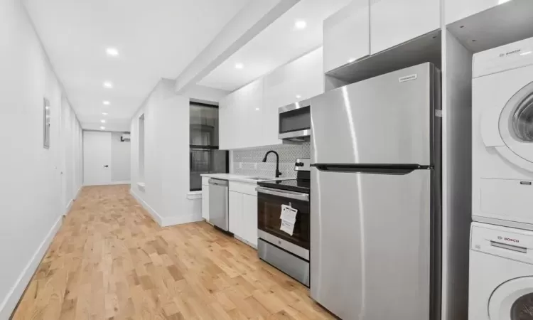 Kitchen with stacked washer and clothes dryer, sink, appliances with stainless steel finishes, tasteful backsplash, and white cabinetry