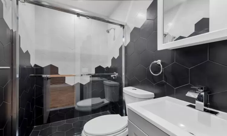 Bathroom with vanity, a shower with door, toilet, and tile walls