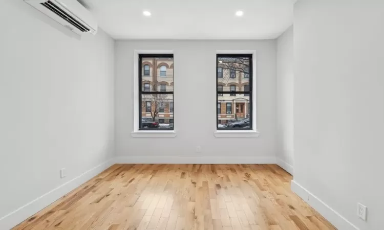 Empty room with a wall unit AC and light hardwood / wood-style floors