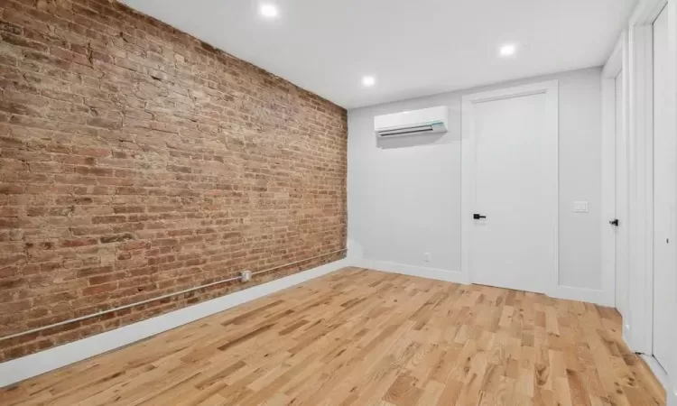 Spare room with a wall unit AC, brick wall, and light hardwood / wood-style floors