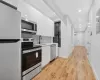 Kitchen featuring sink, stainless steel appliances, decorative backsplash, white cabinets, and light wood-type flooring