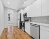 Kitchen with sink, light wood-type flooring, appliances with stainless steel finishes, tasteful backsplash, and white cabinetry