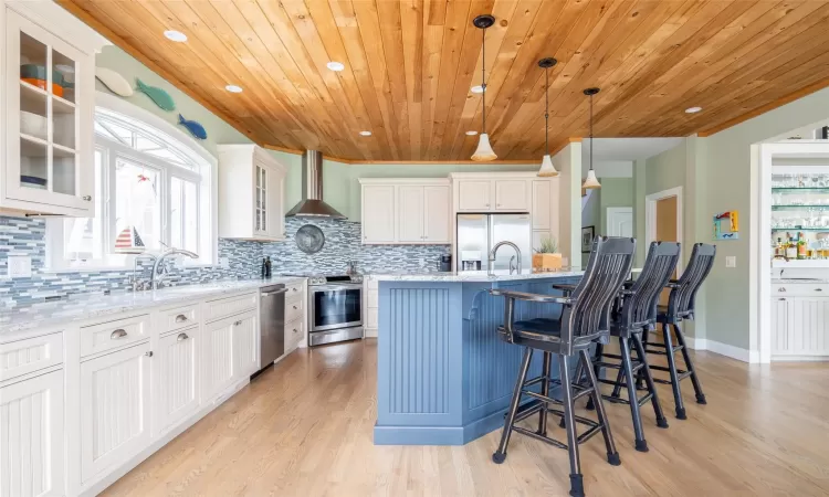 Kitchen featuring white cabinets, decorative light fixtures, wall chimney range hood, and appliances with stainless steel finishes