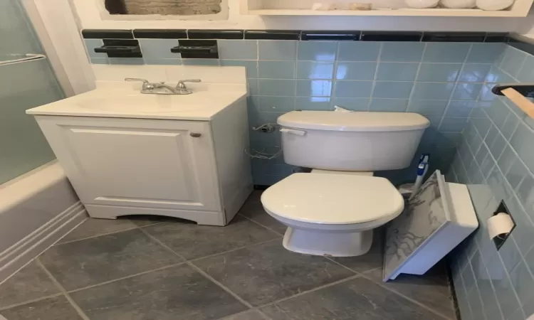 Full bathroom with vanity, toilet, shower / bath combination with glass door, and tile walls