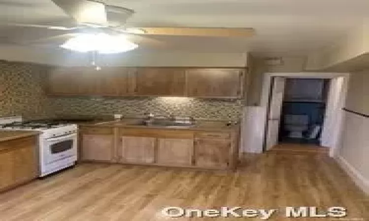 Kitchen featuring tasteful backsplash, gas range gas stove, ceiling fan, sink, and light hardwood / wood-style floors