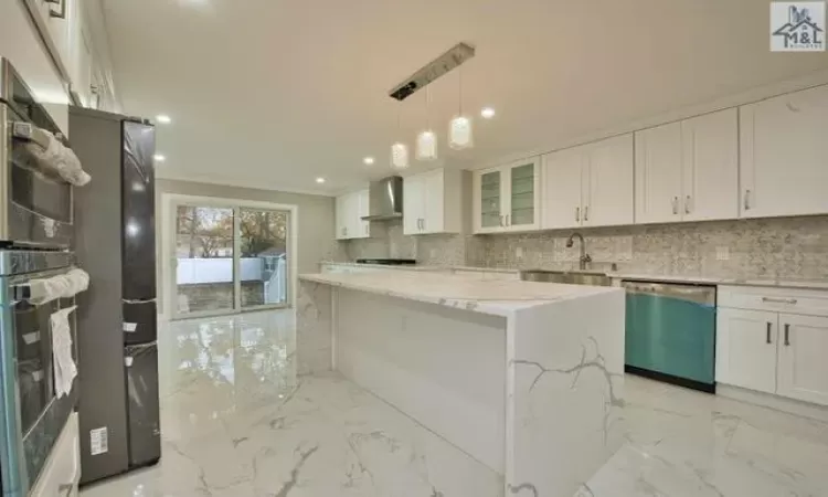 Kitchen featuring light stone countertops, white cabinetry, stainless steel dishwasher, and wall chimney exhaust hood