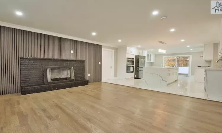 Unfurnished living room featuring a fireplace, ornamental molding, and light wood-type flooring