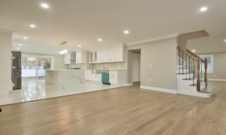 Kitchen with stainless steel dishwasher, crown molding, wall chimney range hood, light hardwood / wood-style flooring, and white cabinetry