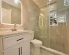 Bathroom with ornamental molding, vanity, a shower with door, tile walls, and toilet