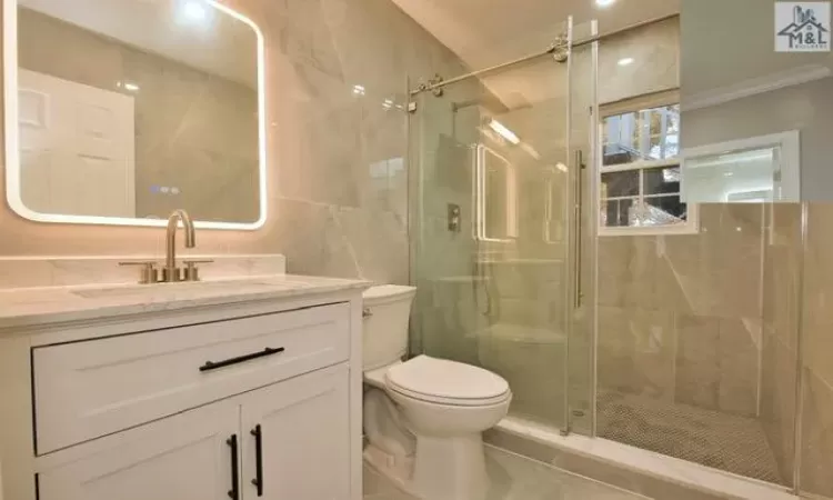 Bathroom with ornamental molding, vanity, a shower with door, tile walls, and toilet