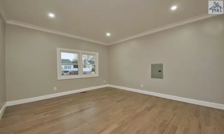 Unfurnished room featuring wood-type flooring, electric panel, and crown molding