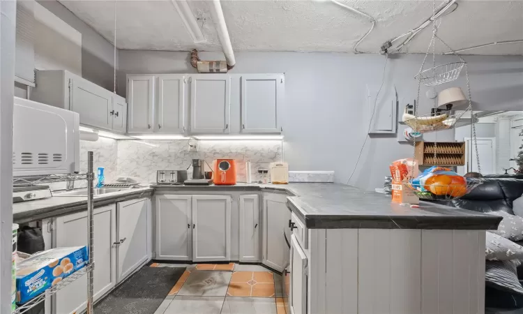 Kitchen featuring kitchen peninsula, decorative backsplash, tile patterned flooring, and white cabinetry