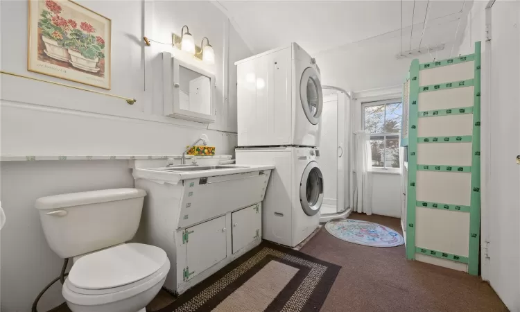 Bathroom featuring vanity, toilet, ornamental molding, and stacked washer / dryer