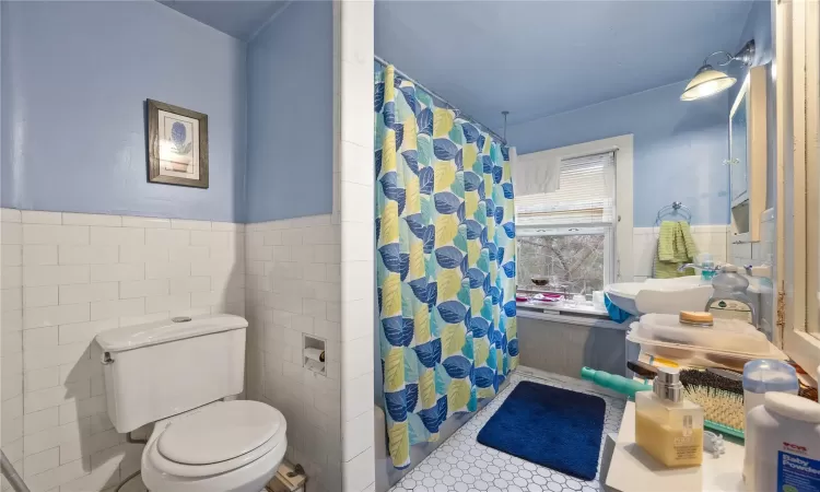 Bathroom featuring tile patterned flooring, toilet, tile walls, and a shower with shower curtain