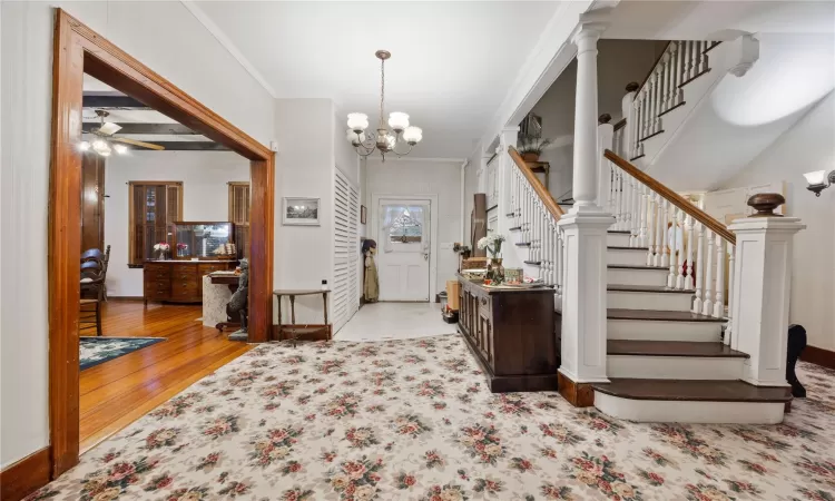 Entrance foyer with decorative columns, light hardwood / wood-style flooring, crown molding, and a notable chandelier