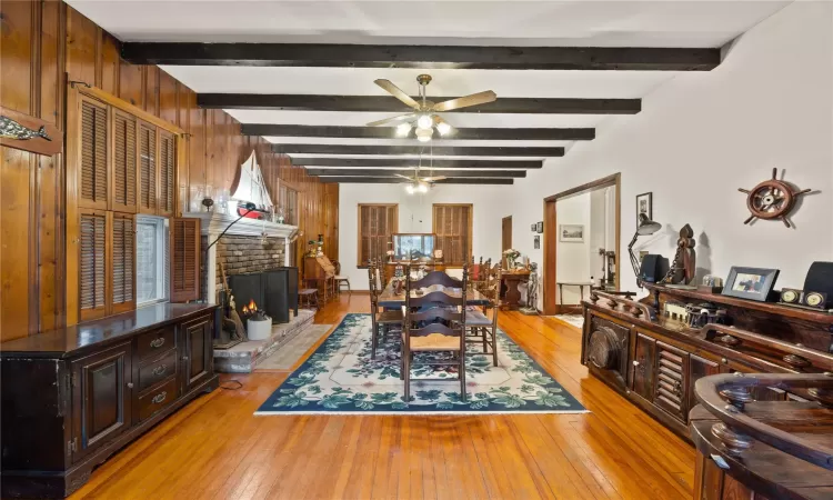 Dining area with beam ceiling, ceiling fan, a brick fireplace, light hardwood / wood-style flooring, and wood walls