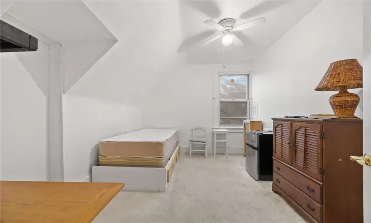 Bedroom featuring ceiling fan, stainless steel fridge, light colored carpet, and lofted ceiling