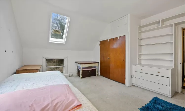 Bedroom with vaulted ceiling with skylight and light colored carpet