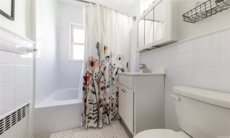 Full bathroom with vanity, shower / bath combo, radiator, toilet, and tile walls