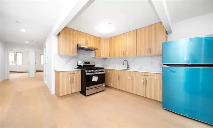 Kitchen featuring sink, light brown cabinets, stainless steel appliances, range hood, and light hardwood / wood-style floors