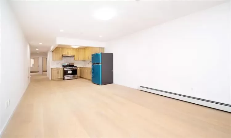 Kitchen with black refrigerator, stainless steel stove, a baseboard radiator, and light wood-type flooring