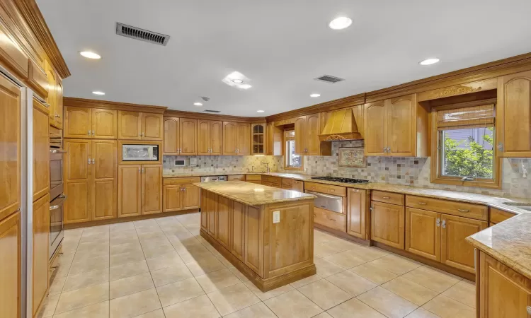 Kitchen with light stone countertops, a center island, stainless steel appliances, light tile patterned floors, and custom exhaust hood