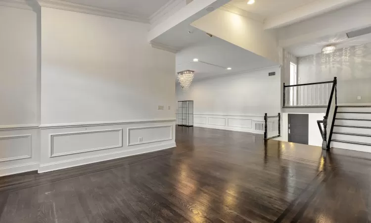 Empty room featuring ornamental molding, an inviting chandelier, and dark wood-type flooring