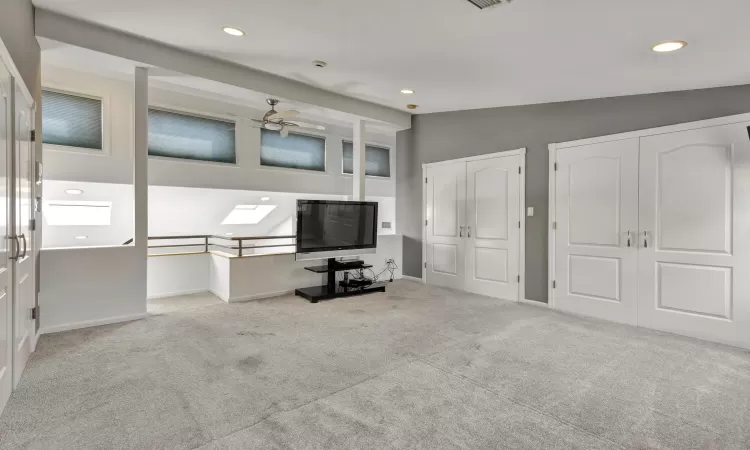 Unfurnished office with ceiling fan, light carpet, and lofted ceiling with skylight