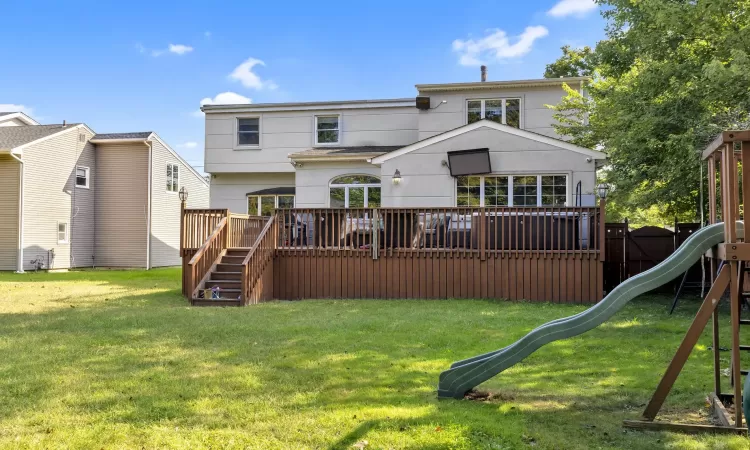 Rear view of house with a playground, a wooden deck, and a lawn