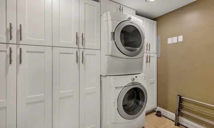 Laundry area with cabinets, stacked washing maching and dryer, and light tile patterned floors