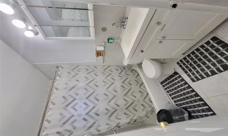 Bathroom featuring tile patterned flooring, vanity, toilet, and tile walls