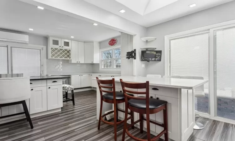 Kitchen with tasteful backsplash, white cabinetry, a breakfast bar area, and a wall mounted air conditioner