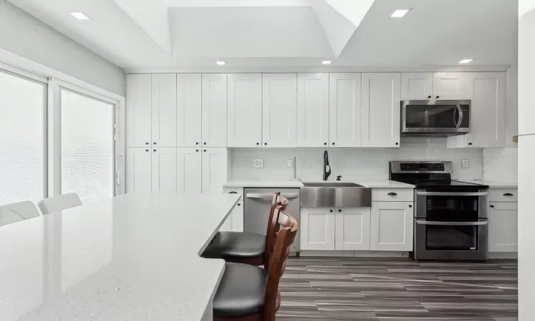 Kitchen featuring a kitchen breakfast bar, sink, white cabinets, and stainless steel appliances