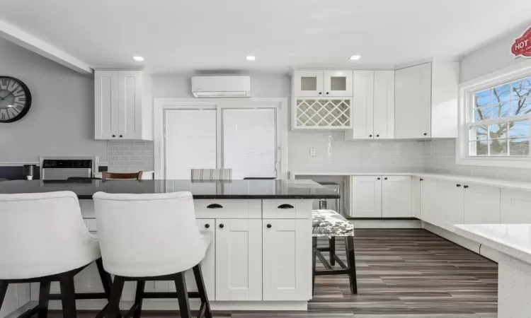 Kitchen featuring a breakfast bar, white cabinetry, backsplash, and an AC wall unit