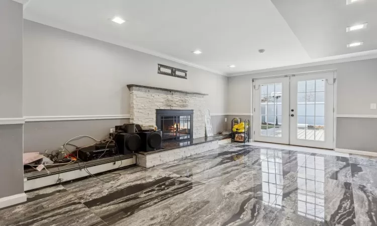 Living room with a baseboard heating unit, a stone fireplace, ornamental molding, and french doors