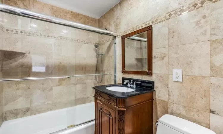 Full bathroom with shower / bath combination with glass door, vanity, toilet, and tile walls