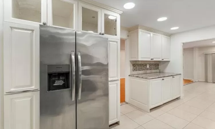 Kitchen with white cabinetry, light stone countertops, stainless steel fridge with ice dispenser, decorative backsplash, and light tile patterned floors