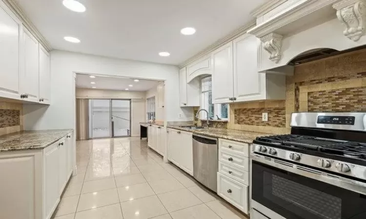 Kitchen with tasteful backsplash, light stone counters, custom range hood, stainless steel appliances, and white cabinetry