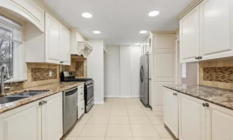 Kitchen featuring appliances with stainless steel finishes, light tile patterned floors, dark stone counters, and sink