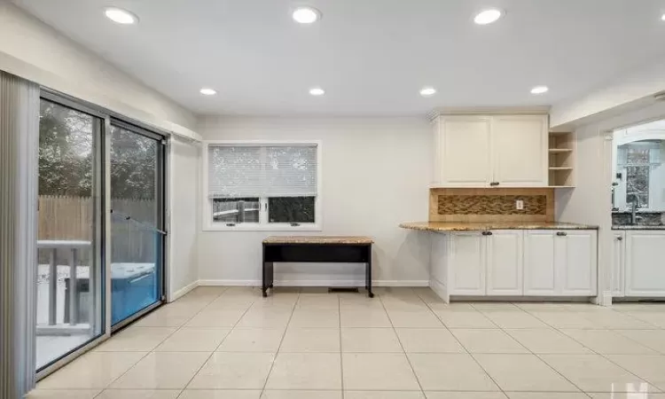 Kitchen featuring white cabinets, decorative backsplash, light tile patterned flooring, and a wealth of natural light