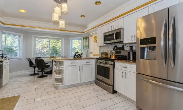 Kitchen featuring white cabinets, appliances with stainless steel finishes, and ornamental molding