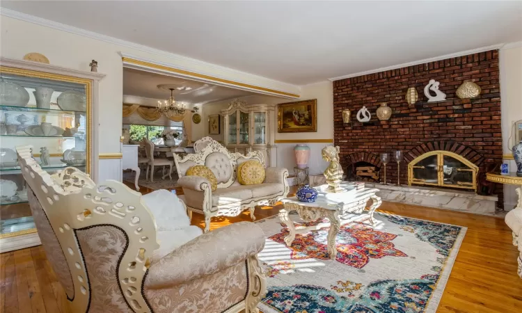 Living room featuring hardwood / wood-style flooring, a chandelier, crown molding, and a brick fireplace