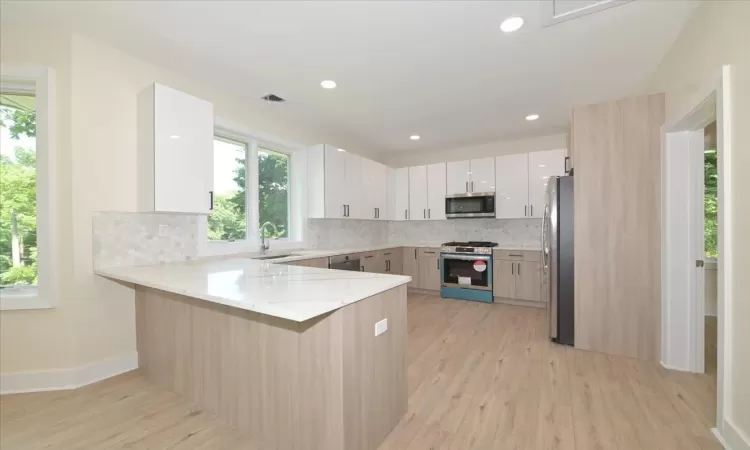 Kitchen featuring sink, stainless steel appliances, tasteful backsplash, kitchen peninsula, and white cabinets