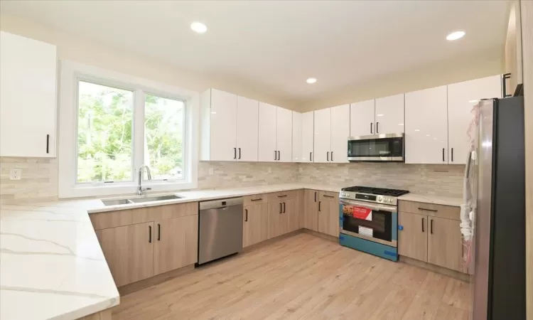 Kitchen with light brown cabinets, sink, decorative backsplash, light stone counters, and stainless steel appliances