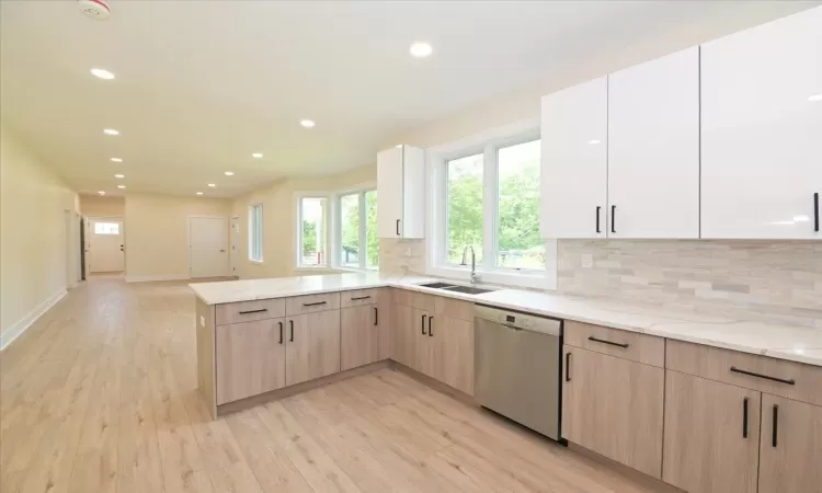 Kitchen with sink, stainless steel dishwasher, light brown cabinetry, tasteful backsplash, and kitchen peninsula