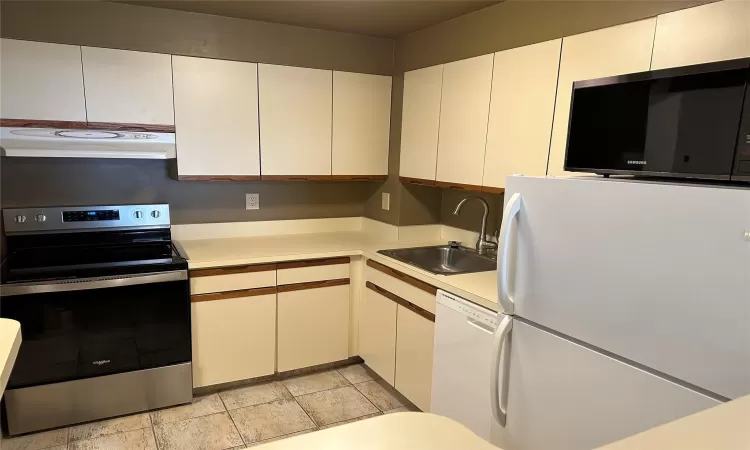 Kitchen with white appliances, white cabinetry, range hood, and sink