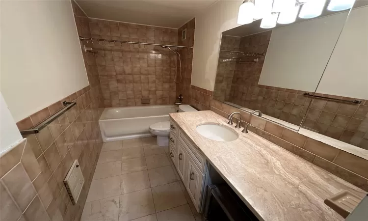 Full bathroom with vanity, tiled shower / bath combo, toilet, and tile walls