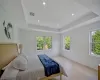 Bedroom featuring a tray ceiling, multiple windows, and light hardwood / wood-style floors