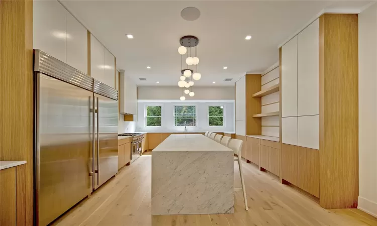 Kitchen featuring high end appliances, white cabinets, a center island, light hardwood / wood-style floors, and hanging light fixtures